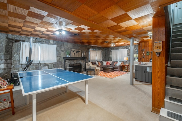 recreation room featuring a stone fireplace, light carpet, sink, and wood ceiling