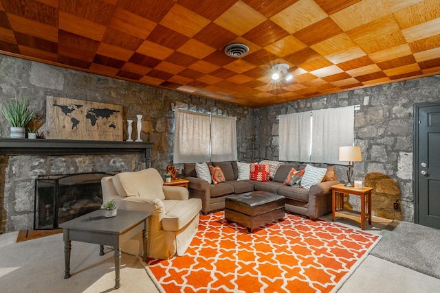 carpeted living room with a stone fireplace and wooden ceiling