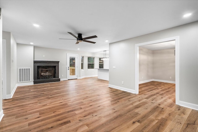 unfurnished living room featuring light wood-type flooring, a brick fireplace, and ceiling fan