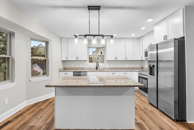 kitchen with a center island, hanging light fixtures, light hardwood / wood-style floors, white cabinetry, and stainless steel appliances