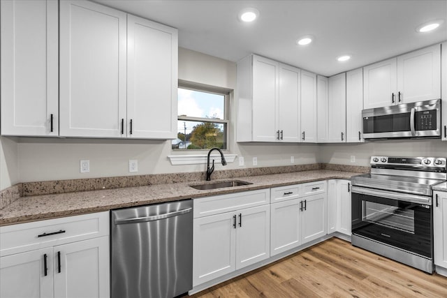 kitchen with light stone counters, stainless steel appliances, sink, light hardwood / wood-style flooring, and white cabinetry