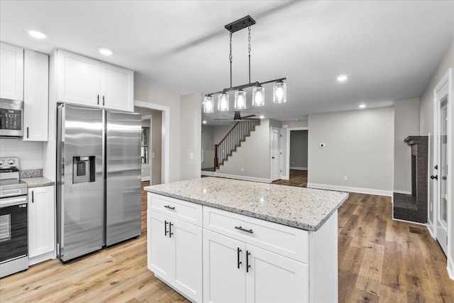 kitchen with light stone countertops, appliances with stainless steel finishes, light wood-type flooring, a kitchen island, and white cabinetry