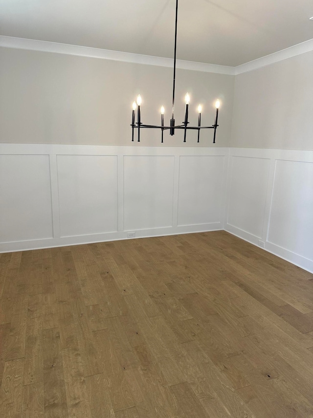 unfurnished dining area with hardwood / wood-style floors, crown molding, and an inviting chandelier