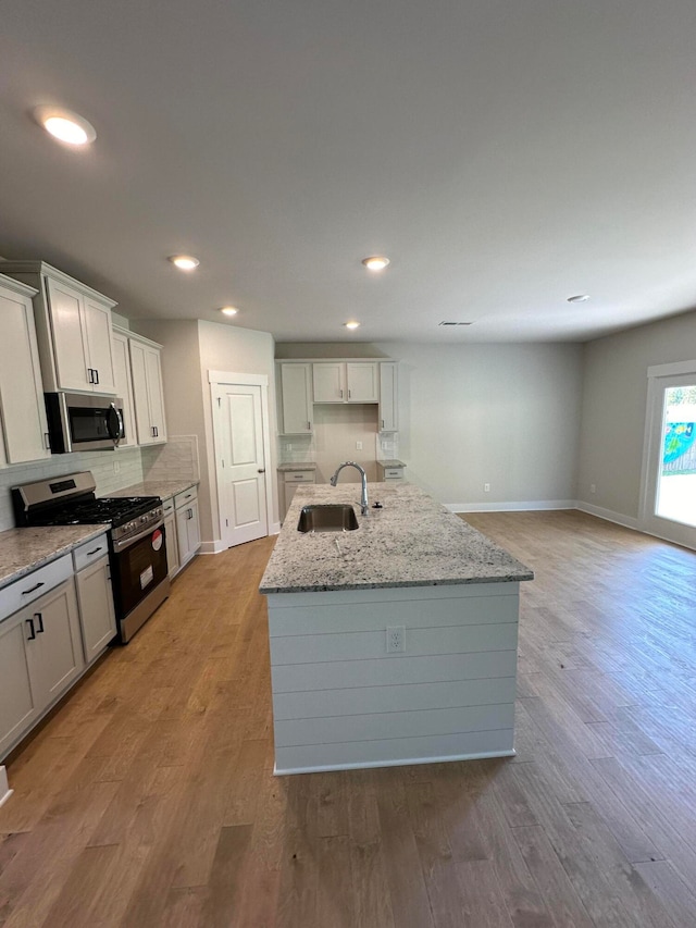 kitchen with sink, light wood-type flooring, a center island with sink, and appliances with stainless steel finishes