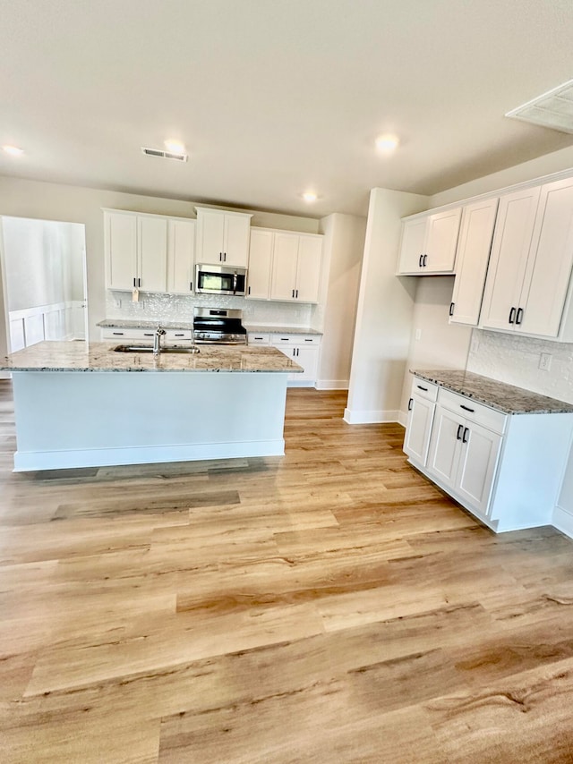 kitchen featuring white cabinets, light hardwood / wood-style floors, a center island with sink, and appliances with stainless steel finishes