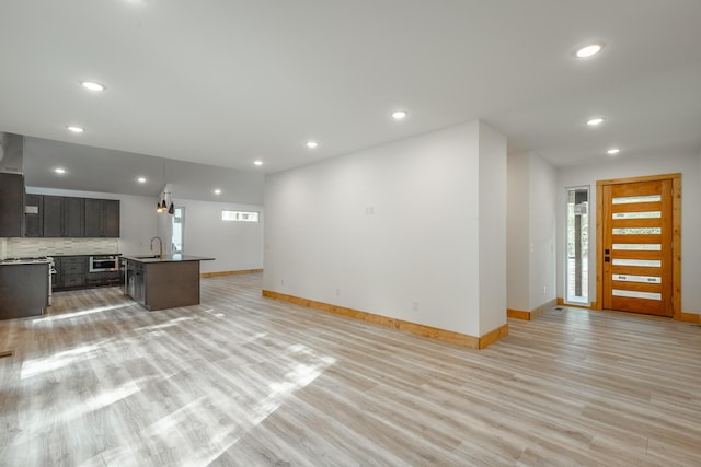 kitchen featuring tasteful backsplash, a kitchen island with sink, sink, light hardwood / wood-style flooring, and hanging light fixtures