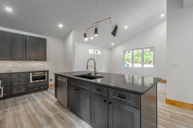 kitchen featuring sink, stainless steel appliances, lofted ceiling, decorative light fixtures, and a center island with sink