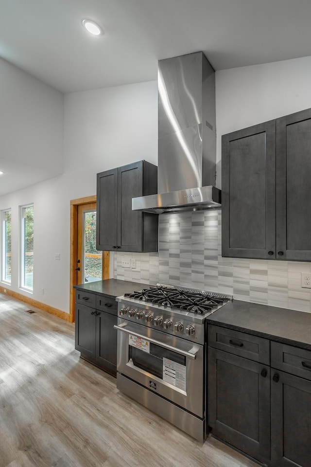 kitchen featuring light hardwood / wood-style floors, high end stove, wall chimney range hood, and tasteful backsplash