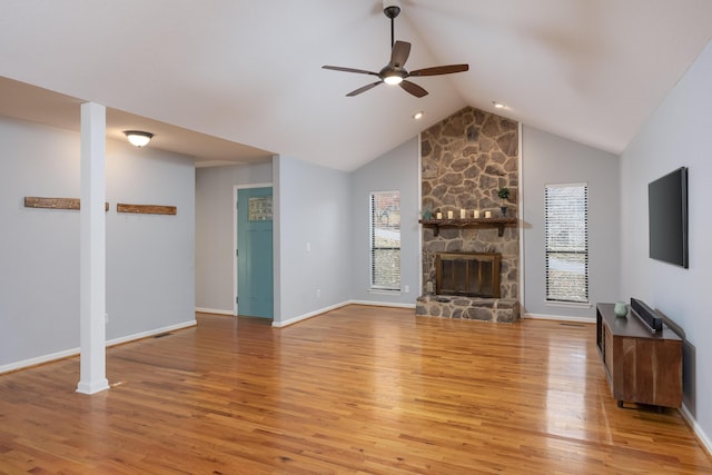 unfurnished living room with ceiling fan, vaulted ceiling, a stone fireplace, and light hardwood / wood-style flooring