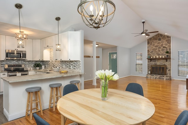 dining room featuring lofted ceiling, ceiling fan with notable chandelier, a stone fireplace, sink, and light wood-type flooring