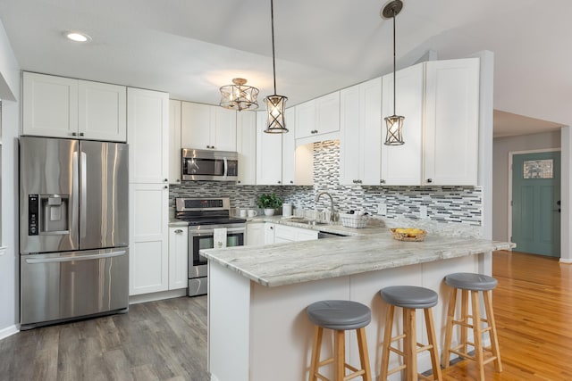 kitchen with sink, hanging light fixtures, stainless steel appliances, light hardwood / wood-style flooring, and white cabinets