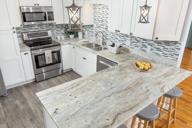 kitchen with a kitchen bar, white cabinetry, hanging light fixtures, and stainless steel appliances