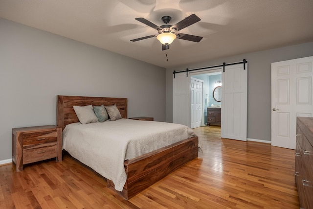 bedroom with ceiling fan, a barn door, light wood-type flooring, and connected bathroom