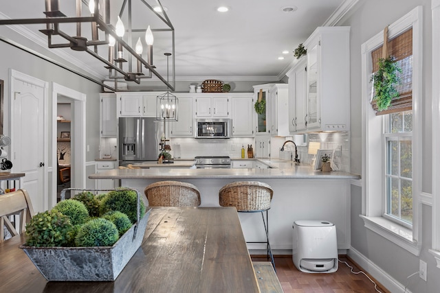 kitchen featuring pendant lighting, white cabinets, appliances with stainless steel finishes, a kitchen bar, and ornamental molding