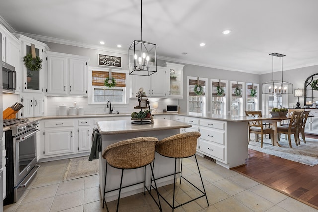 kitchen with appliances with stainless steel finishes, white cabinets, light tile patterned floors, a breakfast bar, and a kitchen island