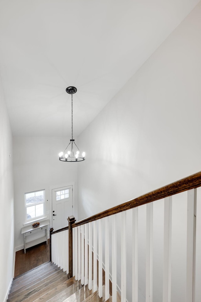 stairs featuring hardwood / wood-style floors, a notable chandelier, and vaulted ceiling