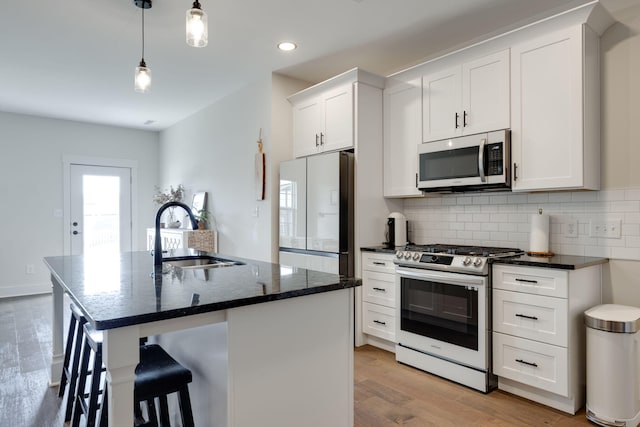 kitchen featuring a kitchen island with sink, white cabinets, sink, light hardwood / wood-style floors, and stainless steel appliances