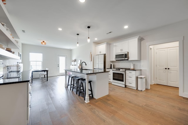 kitchen with white cabinetry, stainless steel appliances, light hardwood / wood-style flooring, an island with sink, and pendant lighting