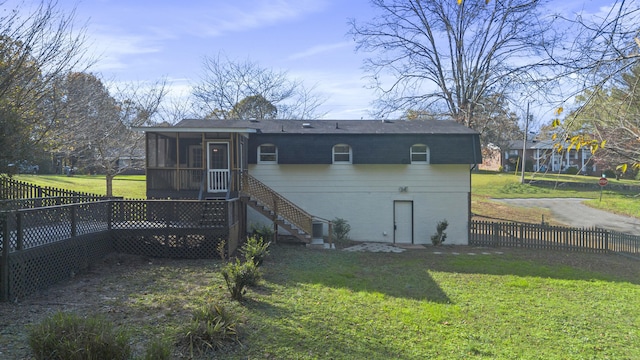 rear view of property featuring a lawn, a sunroom, and a deck