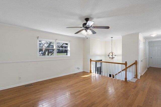 empty room with a textured ceiling, ceiling fan with notable chandelier, hardwood / wood-style flooring, and crown molding