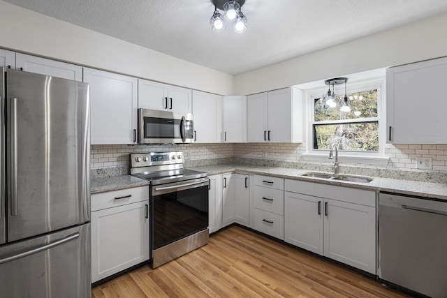 kitchen with white cabinetry, sink, tasteful backsplash, light hardwood / wood-style flooring, and appliances with stainless steel finishes