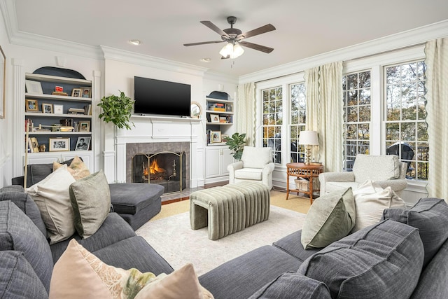 living room featuring built in shelves, a wealth of natural light, crown molding, and a tiled fireplace