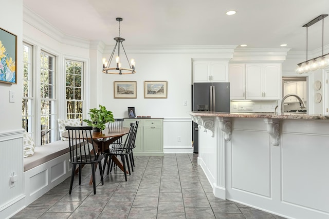 kitchen with hanging light fixtures, an inviting chandelier, a breakfast bar area, white cabinets, and ornamental molding