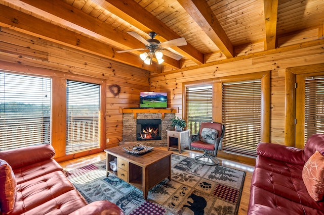 living room with beam ceiling, hardwood / wood-style flooring, a stone fireplace, and wooden walls