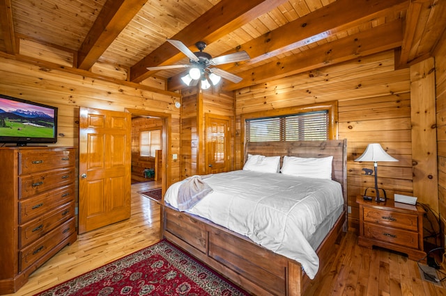 bedroom with ceiling fan, beamed ceiling, wood walls, wood ceiling, and light wood-type flooring