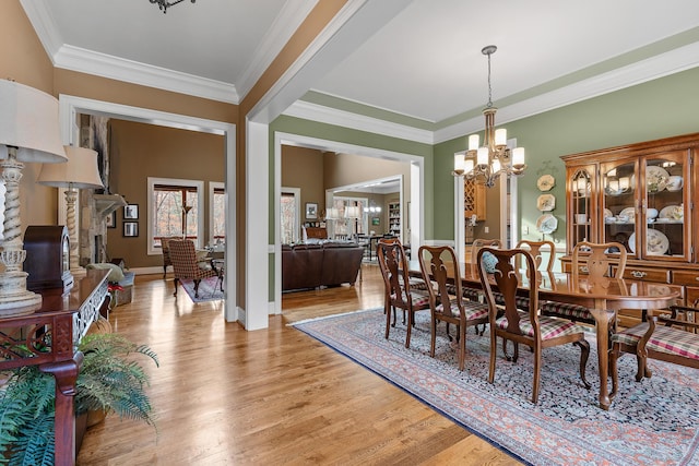 dining space featuring a chandelier, ornamental molding, light hardwood / wood-style flooring, and a stone fireplace