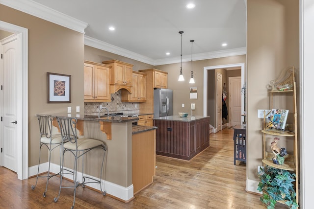 kitchen with hanging light fixtures, stainless steel appliances, light hardwood / wood-style flooring, kitchen peninsula, and dark stone counters