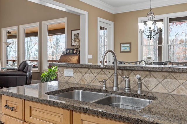 kitchen featuring ornamental molding, dark stone counters, sink, a chandelier, and hanging light fixtures