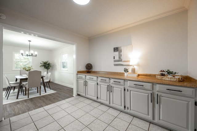 kitchen with crown molding, light hardwood / wood-style flooring, hanging light fixtures, and a notable chandelier