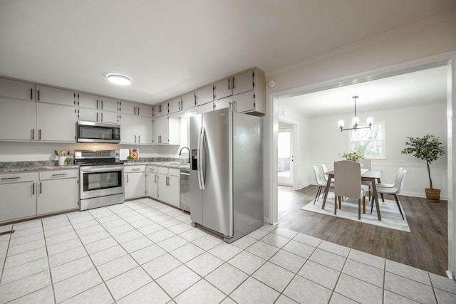 kitchen featuring sink, light wood-type flooring, ornamental molding, decorative light fixtures, and stainless steel appliances