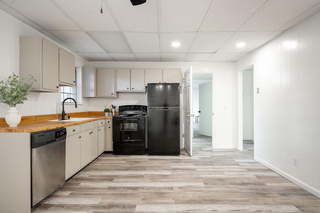 kitchen featuring wooden counters, a paneled ceiling, sink, black appliances, and light hardwood / wood-style flooring