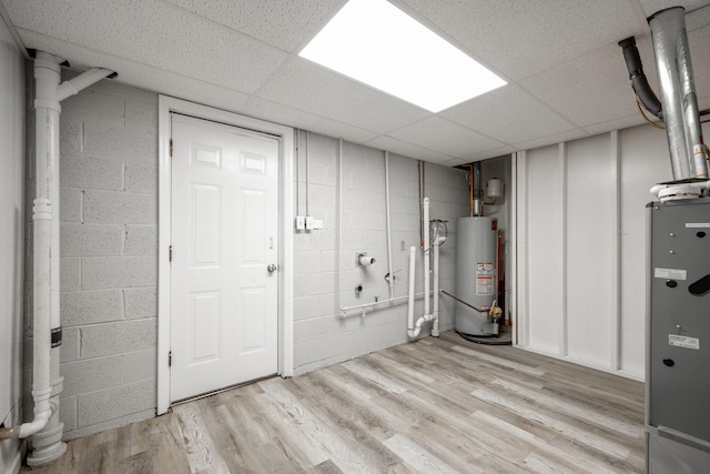 basement with a drop ceiling, water heater, and light hardwood / wood-style flooring