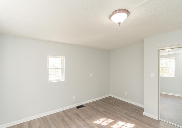 unfurnished room with plenty of natural light, wood finished floors, baseboards, and a textured ceiling