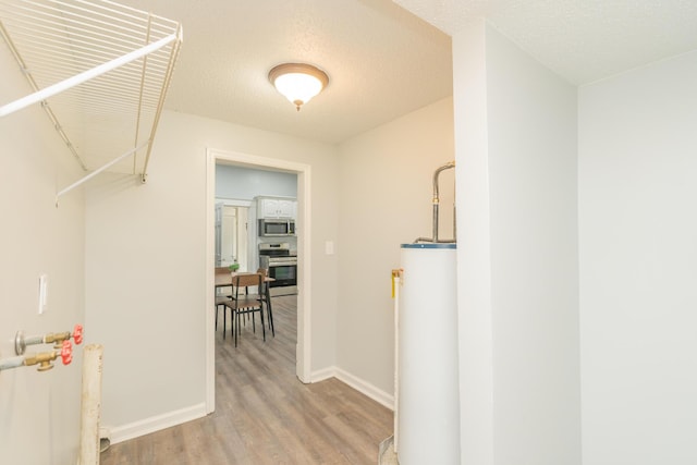 hallway featuring gas water heater, light wood-type flooring, baseboards, and a textured ceiling