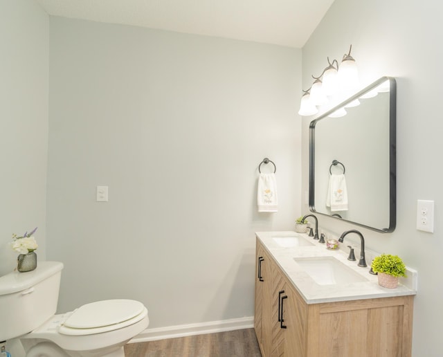 bathroom with toilet, baseboards, wood finished floors, and double vanity