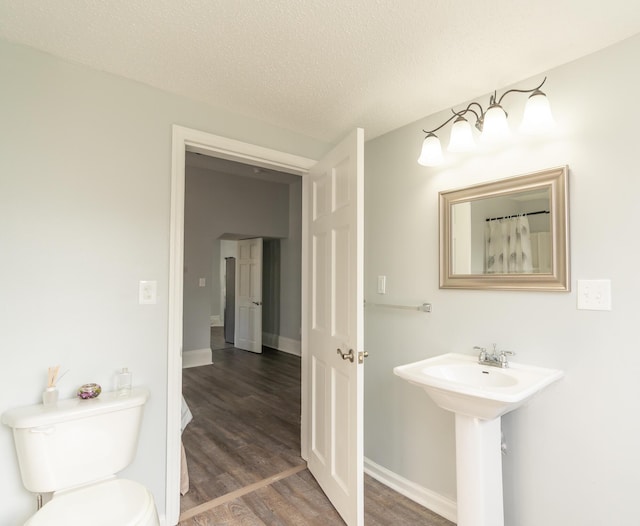 bathroom featuring wood finished floors, toilet, a textured ceiling, baseboards, and a sink