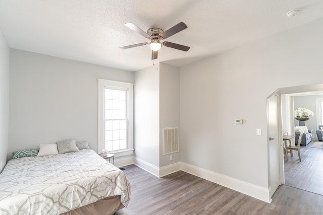 bedroom with wood finished floors, baseboards, arched walkways, a ceiling fan, and a textured ceiling