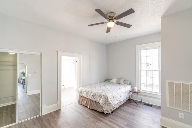 bedroom featuring a textured ceiling, dark hardwood / wood-style flooring, a closet, and ceiling fan