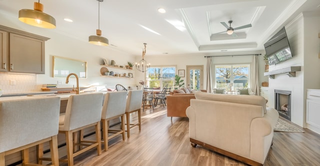 living room featuring a tray ceiling, crown molding, light hardwood / wood-style floors, and ceiling fan with notable chandelier