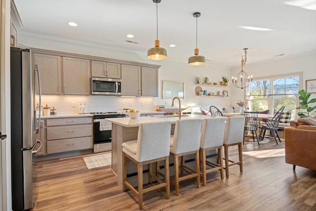 kitchen featuring stainless steel appliances, sink, wood-type flooring, pendant lighting, and a center island with sink