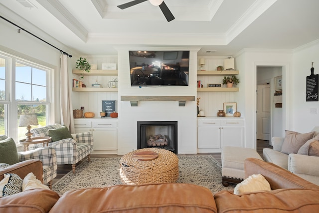 living room featuring a fireplace, light hardwood / wood-style floors, a raised ceiling, and ornamental molding