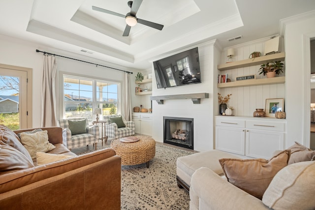 living room featuring ceiling fan, a raised ceiling, ornamental molding, and a fireplace