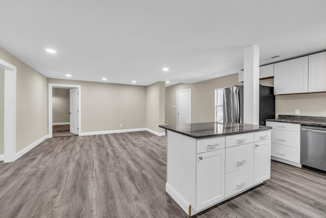 kitchen with stainless steel appliances, white cabinetry, dark stone counters, and light hardwood / wood-style flooring