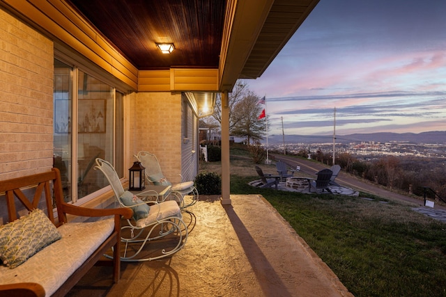 patio terrace at dusk with a lawn, a mountain view, and a fire pit