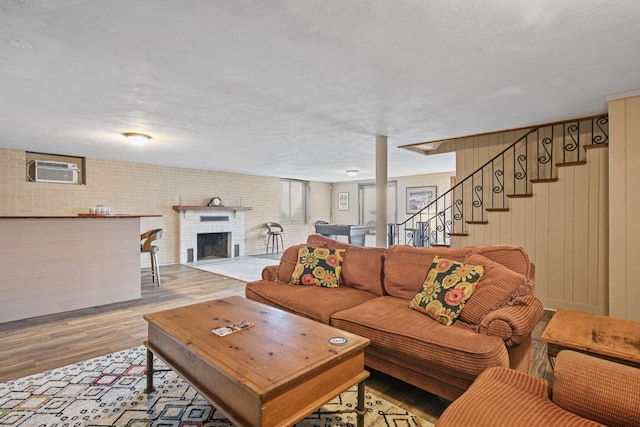 living room with a wall mounted AC, wood walls, light hardwood / wood-style floors, a textured ceiling, and a fireplace