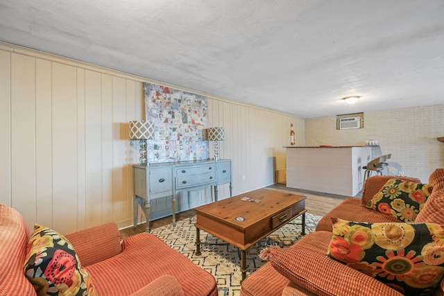 living room featuring a textured ceiling, light hardwood / wood-style floors, an AC wall unit, and wooden walls